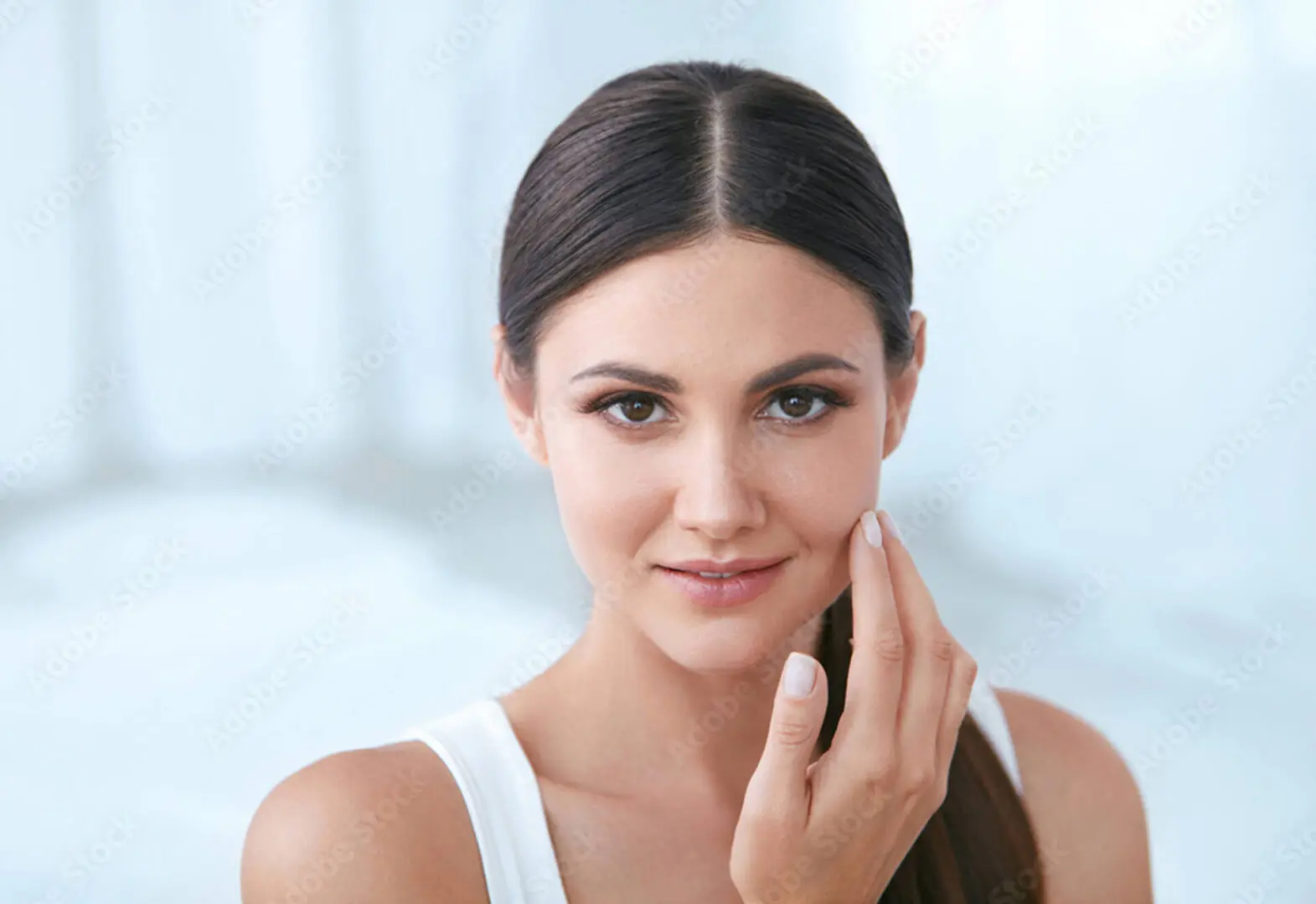 A woman with long dark hair and a white tank top gently touches her cheek, showcasing the serene essence of bioenergy healing as she gazes at the camera.