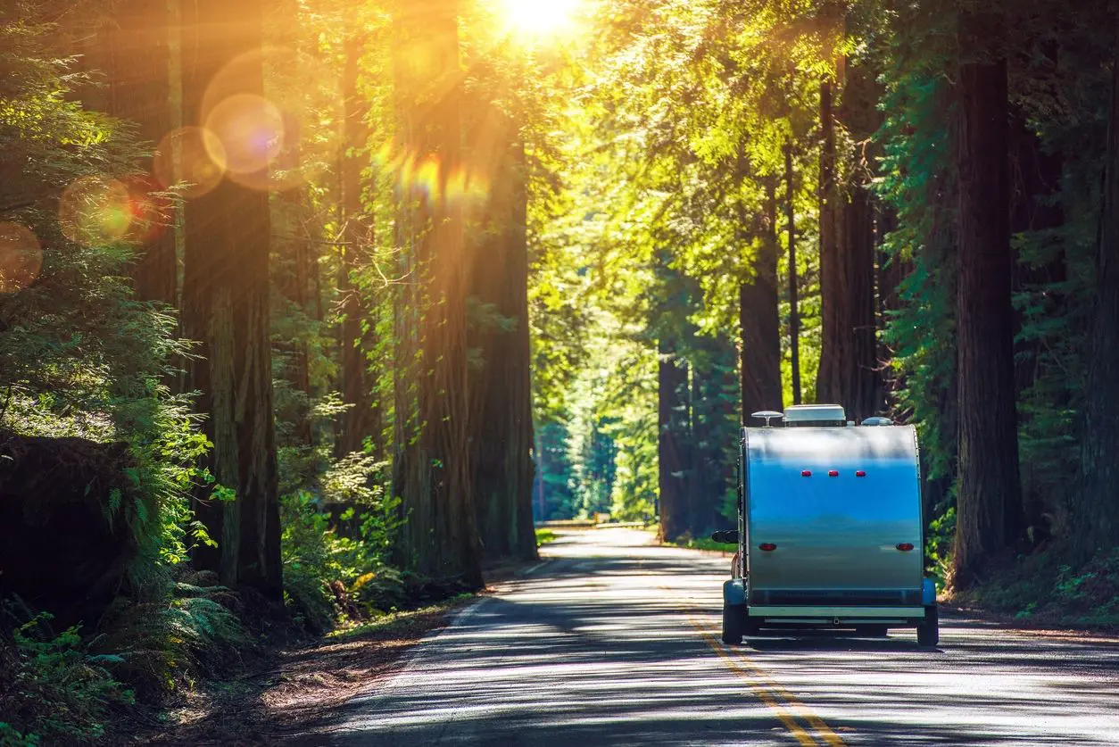 A camper trailer driving down the road in the woods.
